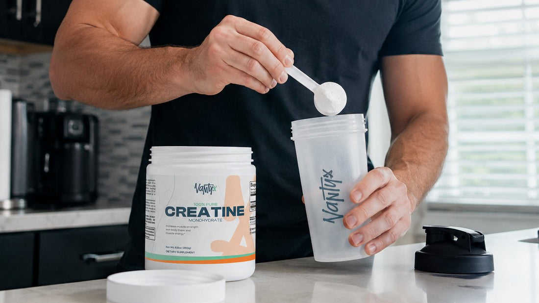 Scooping a 5 g serving of creatine monohydrate powder from an open tub into a shaker on a kitchen counter