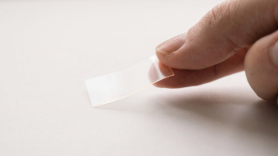 A single translucent Vantyx oral energy strip held at a fingertip on a paper-white surface in soft daylight, showing the format that carries 50mg of caffeine